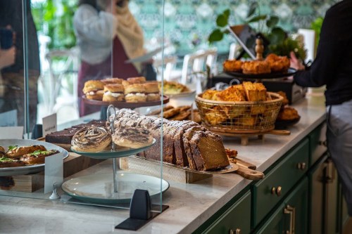 A display of assorted baked goods, including cakes, pastries, and bread, in a cozy café setting.