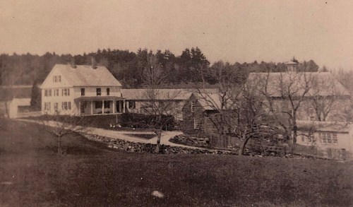 Black and white photo of a large farmhouse and barn, surrounded by trees and a grassy area.