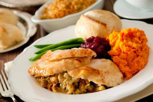 A plate of Thanksgiving dinner featuring turkey, stuffing, sweet potatoes, green beans, cranberry sauce, and rolls.