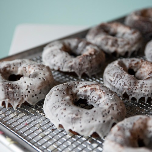 A tray of freshly glazed donuts with a speckled icing, resting on a wire cooling rack.
