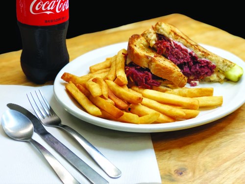 A plate with a sandwich filled with meat, served with fries and a bottle of Coca-Cola on the side.