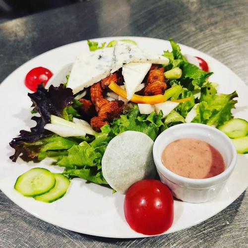A colorful salad with greens, sliced cucumbers, cherry tomatoes, and blue cheese, served with a creamy dressing.