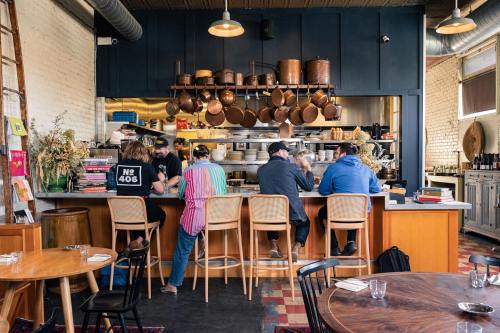A cozy restaurant interior with patrons seated at a bar, surrounded by hanging pots and a vibrant kitchen backdrop.