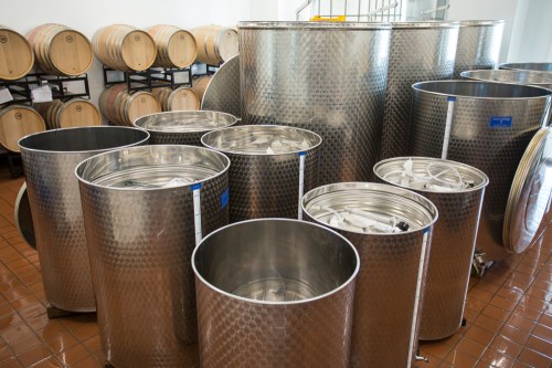 Stainless steel fermentation tanks and barrels in a winery storage area.