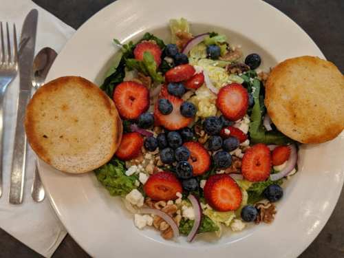 A colorful salad with greens, strawberries, blueberries, nuts, and two toasted bread slices on the side.
