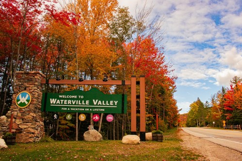 A welcome sign for Waterville Valley surrounded by vibrant autumn foliage and a clear blue sky.