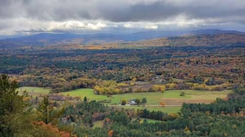 A scenic view of rolling hills and valleys, showcasing vibrant autumn foliage under a cloudy sky.