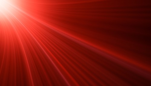Abstract red background with radiant light beams creating a dynamic, flowing pattern.