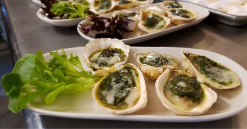 A plate of baked oysters topped with green sauce, accompanied by fresh lettuce and salad greens.