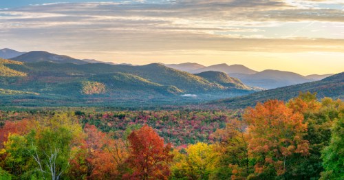 A vibrant landscape of rolling hills and mountains, adorned with colorful autumn foliage under a golden sunset.