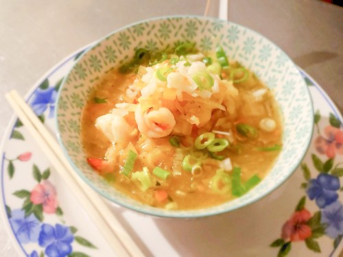 A bowl of soup with shrimp, green onions, and vegetables, served with chopsticks on a decorative plate.
