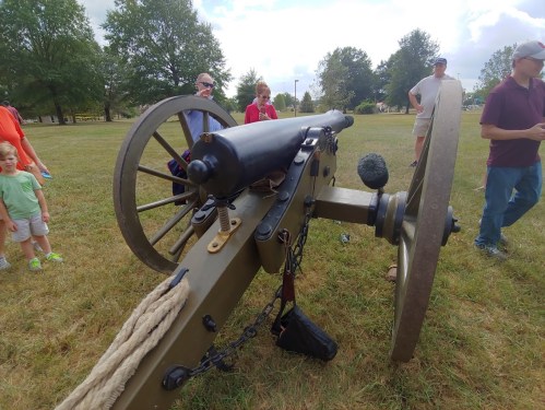 A historic cannon on display, with people observing in a grassy area under a cloudy sky.