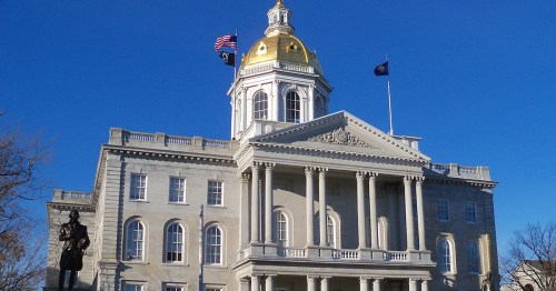 New Hampshire State House with a golden dome, flags flying, and a clear blue sky in the background.
