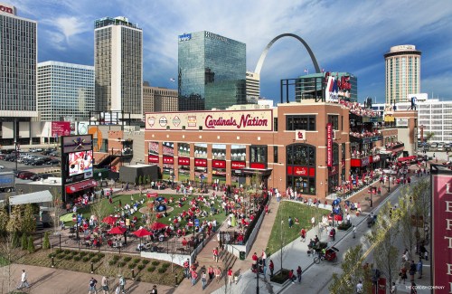 A vibrant outdoor area with fans in red, surrounded by buildings and the Gateway Arch in St. Louis, Missouri.