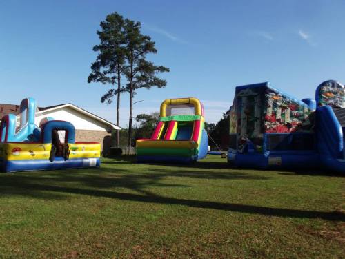 Colorful inflatable bounce houses set up on a grassy area under a clear blue sky.