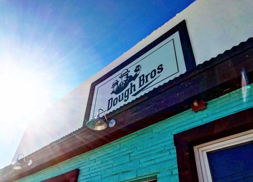Sign for "Dough Bros" on a turquoise building, with sunlight shining brightly in the background.