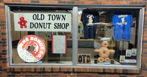 Window display of Old Town Donut Shop featuring colorful signs, t-shirts, and a large donut decoration.