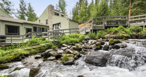 A serene scene of a building by a flowing stream, surrounded by lush greenery and trees.