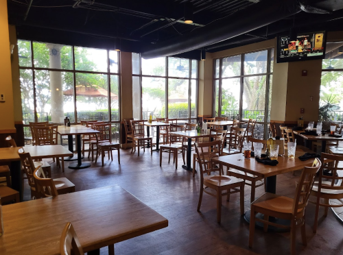 A spacious restaurant interior with wooden tables and chairs, large windows, and a few empty glasses on the tables.
