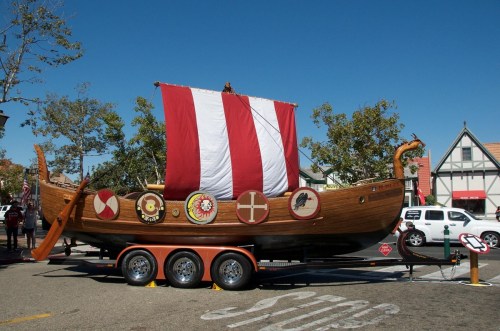A decorative wooden Viking ship on a trailer, featuring a red and white sail and various shields on its sides.