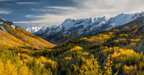 A stunning mountain landscape with snow-capped peaks and vibrant autumn foliage in shades of yellow and green.