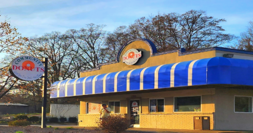 A donut shop with a blue awning and a sign, surrounded by trees and a clear sky.