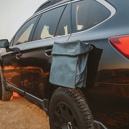 A black SUV with a Luno storage bag attached to its side, parked on a dirt road during sunset.