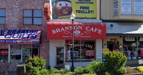 A street view of Branson Cafe with a red awning, surrounded by shops and a large advertisement for a trolley service.