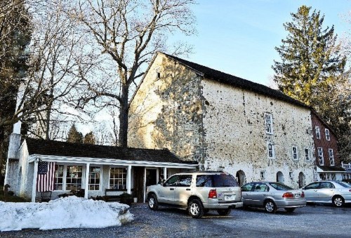 Historic stone building with a red side, parked cars, and snow in the foreground under a clear blue sky.