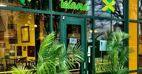 A vibrant restaurant entrance with green plants, large windows, and an "OPEN" sign. Bright colors and tropical decor.