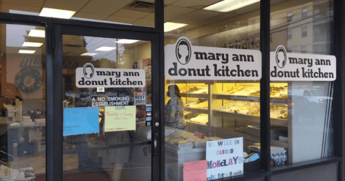 Exterior of Mary Ann Donut Kitchen, featuring large signs and a display of donuts visible through the window.