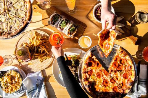 A table spread with pizza, tacos, fries, burgers, and drinks, with hands reaching for food.