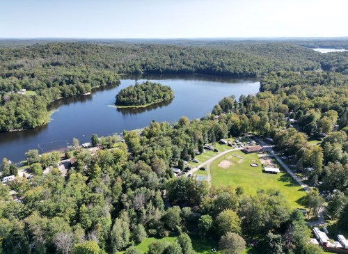 Aerial view of a serene lake surrounded by lush greenery and a small island, with a park area visible nearby.