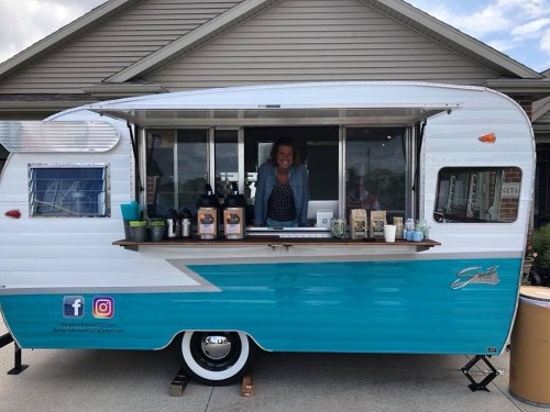 A vintage-style food truck with a smiling vendor serving drinks and snacks from a window.