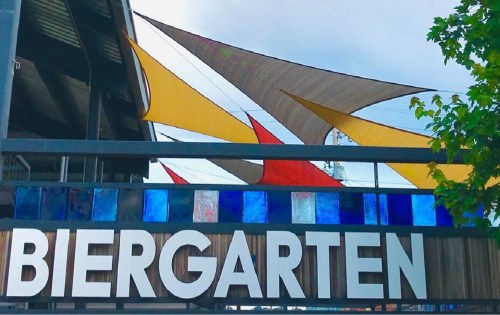 A colorful sign reading "Biergarten" with vibrant sail-like canopies above.