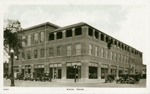 Historic brick building in Waco, Texas, with vintage cars parked outside, captured in a sepia-toned postcard style.