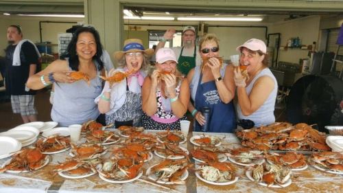 A group of six women joyfully eating crabs at a seafood gathering, with a table full of crabs in front of them.
