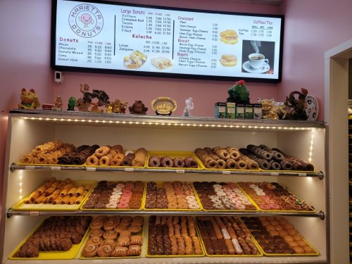 A display case filled with various donuts and pastries, with a menu board overhead listing items and prices.