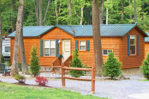 A cozy log cabin surrounded by trees, featuring a green metal roof and a gravel pathway.