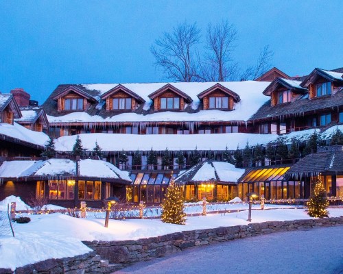 A cozy lodge covered in snow, with icicles hanging from the roof and festive lights illuminating the entrance.