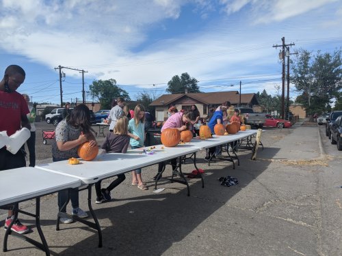 A group of people carving pumpkins at a long table outdoors on a sunny day.