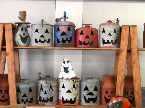 A shelf displays various metal containers painted as Halloween pumpkins and ghosts, featuring playful faces.