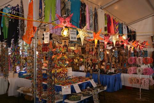 Colorful market stall filled with handmade crafts, jewelry, and decorations under a tent, with vibrant fabrics hanging above.