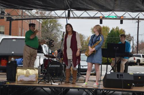 A band performs on stage under a tent, featuring a singer, saxophonist, and musicians with instruments.