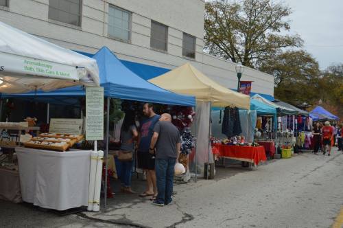 A street market scene with colorful tents, vendors, and shoppers browsing various goods.