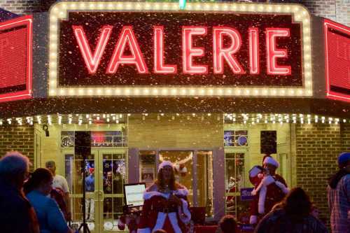 A festive theater marquee reading "VALERIE" with snow falling and people in holiday attire outside.