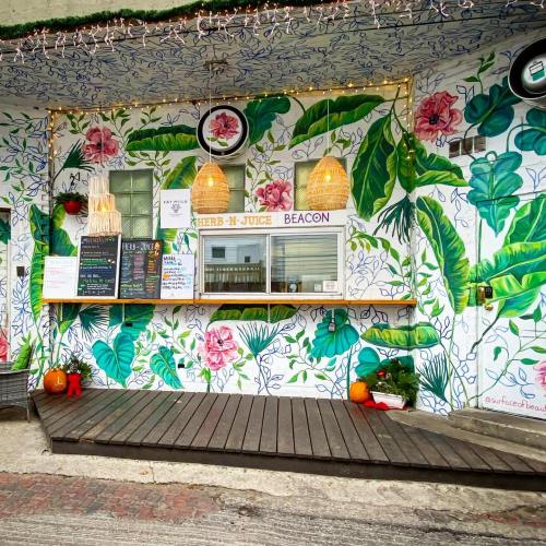 Colorful mural with tropical plants and flowers on a café wall, featuring a service window and wooden deck.