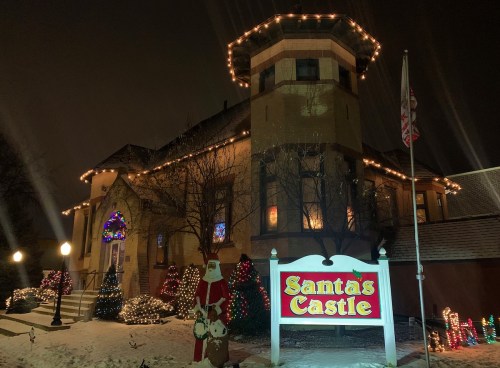 A festive building decorated with Christmas lights, featuring a sign that reads "Santa's Castle" and a Santa figure outside.