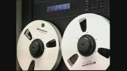 Close-up of two large reel-to-reel tape reels with a digital display showing the time 2129:73.