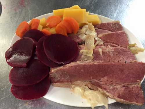 A plate of sliced corned beef with pickled beets, carrots, and yellow squash.